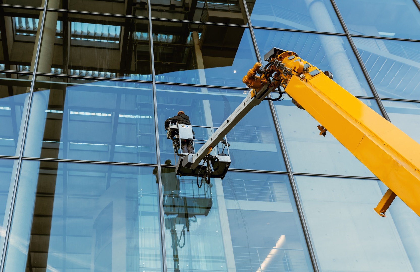 Arbeiter auf einer Hebebuehne reinigt die Glasfassade eines modernen Buerogebaeudes