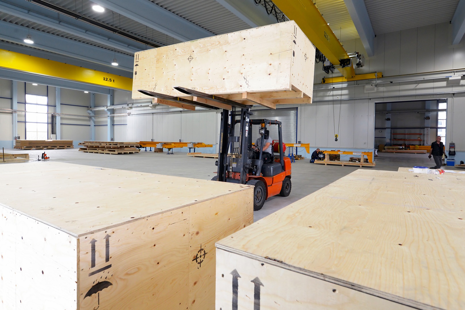 Forklift truck moves large wooden crate with goods in an industrial hall